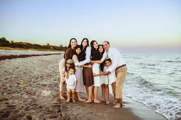 Large family group enjoying a beach photo shoot in Boca Raton with turquoise ocean and golden sand in the background